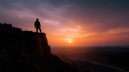 Silhouette of a person standing on a rugged cliff edge observing the vast dramatic landscape bathed in the vibrant colors of a sunset sky