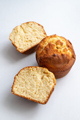 Two muffins on a white surface, one cut in half. The muffins are golden brown and have a slightly crispy texture. Homemade baking and pastry made from wheat flour. Making bread and Easter cakes