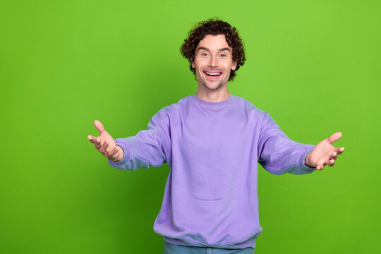 Cheerful young man in purple sweatshirt gesturing openly against vibrant green background celebrating positive emotions