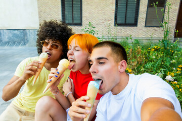 Fototapeta premium Three joyful friends enjoying ice cream cones and taking a selfie