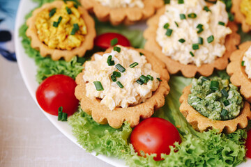 Mini tartlets filled with salad made from eggs and vegetables. Garnished with green onion on lettuce and cherry tomatoes. Homemade appetizer. Traditional party snack. Delicious festive food detail.
