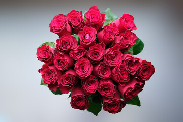 A tight cluster of two dozen red roses form a vibrant bouquet. Green leaves peek out from the bottom of the roses
