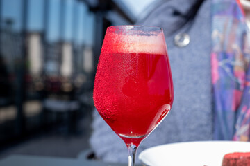 Vibrant red cocktail served in elegant glass, showcasing refreshing bubbles and condensation, set against a blurred outdoor dining backdrop with inviting atmosphere