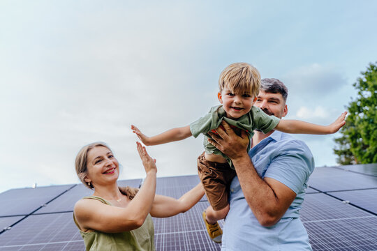 Parents holding son like airplane near solar panels outdoors renewable family life