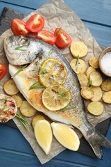 Tasty roasted dorado fish with vegetables and spices on blue wooden table, flat lay. Homemade seafood dish