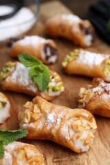 Delicious cannoli with cheese, nuts, powdered sugar and mint on table, closeup