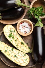 Halves of fresh eggplant, whole ones, spices and parsley on wooden table, flat lay