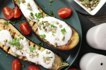 Slices of grilled eggplant with pumpkin seeds, tomatoes and yoghurt on wooden table, flat lay