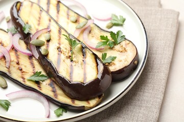 Slices of grilled eggplant, parsley, pumpkin seeds and onion on white table, closeup