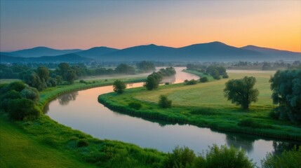 Obraz premium Tranquil natural landscape at dawn or dusk with a meandering river reflecting warm sky hues, lush green banks,