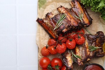 Roasted beef ribs with rosemary, tomatoes and other products on white tiled table, flat lay. Space for text