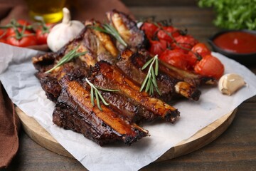 Roasted beef ribs with spices and tomatoes on wooden table, closeup