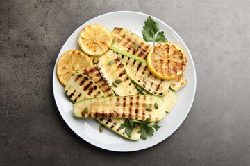 Delicious grilled courgette slices with pumpkin seeds, lemon and parsley on grey textured table, top view