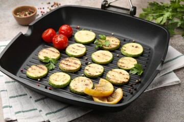 Delicious grilled courgette slices with tomatoes, lemon and parsley in pan on grey textured table, closeup