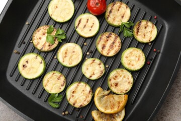 Delicious grilled courgette slices with tomatoes, lemon and parsley in pan on grey textured table, top view