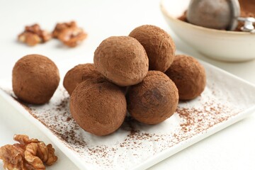 Tasty chocolate candies with cocoa powder and walnuts on white table, closeup