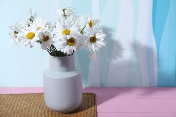 Beautiful chamomile flowers in vase on pink wooden table against color background, closeup. Space for text