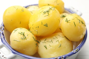 Tasty young boiled potatoes with dill and oil in bowl on white table, closeup
