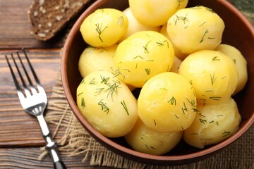Tasty young boiled potatoes with dill and oil in bowl on wooden table, above view