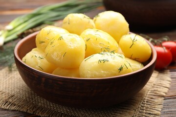 Tasty young boiled potatoes with dill and oil in bowl on wooden table, closeup