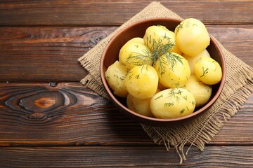 Tasty young boiled potatoes with dill in bowl on wooden table, above view. Space for text