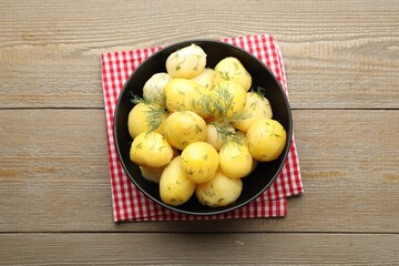 Tasty young boiled potatoes with dill and oil in bowl on wooden table, top view