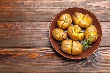 Tasty baked potatoes with rosemary served on wooden table, top view. Space for text