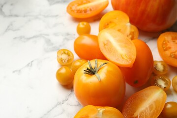 Whole and cut yellow tomatoes on white marble table, closeup. Space for text