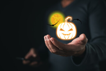 A person holds glowing Halloween-themed icons including a carved pumpkin, bats, and full moon, symbolizing spooky celebration, autumn festivity, and traditional Halloween night atmosphere.