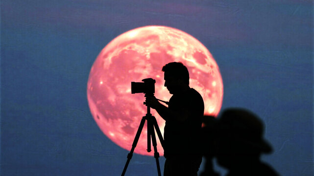 Red Moon Capturing the celestial wonder, a silhouette photographer frames a dramatic, vibrant red moon against a deep twilight sky, inspiring awe and cosmic exploration. - Powered by Adobe