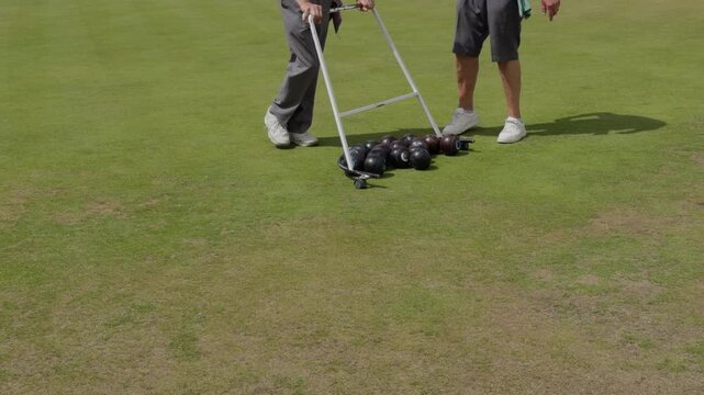 Closeup of two croquet players gathering balls with wheeled hoop device