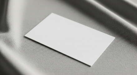 A blank white rectangular card resting on a soft grey textured surface with subtle shadows and draped fabric.