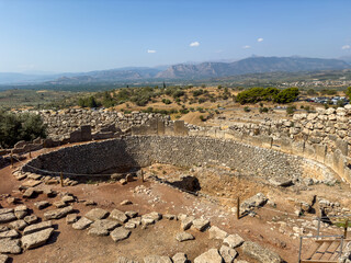 Ancient stone grave circle ruins at Mycenae archaeological site, Greece. Surrounding hills, olive groves, and distant mountain landscape