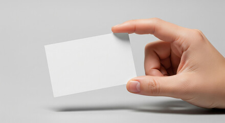 Obraz premium A hand holding a blank white business card or credit card against a light grey background, ready for customization.