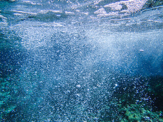 Dark blue ocean surface seen from underwater. Abstract waves underwater and rays of sunlight shining through, Sun light rays undersea deep, Underwater background with sea bottom, Mediterranean sea.
