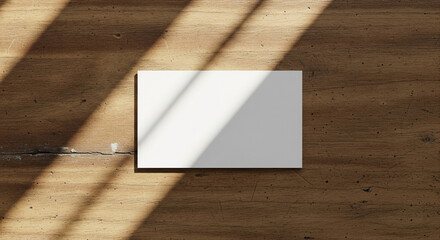 A blank white rectangular card resting on a warm wooden surface with strong linear shadows.