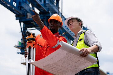 Surveyors and civil engineers using a theodolite and road construction plans to measure and inspect during the building process.