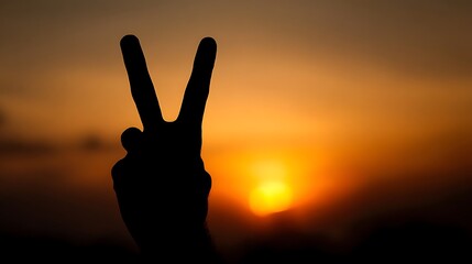 Silhouette of a hand making a peace sign against a vibrant sunset