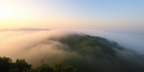 Obraz premium Misty mountain peak covered in fog during a serene sunrise with soft golden light