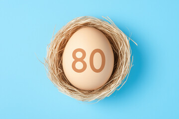 A close-up shot of an egg with the number 80 printed on its surface, nestled comfortably within a woven nest, symbolizing themes of aging and milestones. 