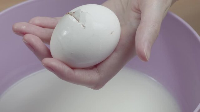 Close-up of woman cracking a chicken egg over a bowl of kefir for dough preparation in her kitchen, recorded with ambient sound.