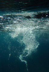 Dark blue ocean surface seen from underwater. Abstract waves underwater and rays of sunlight shining through, Sun light rays undersea deep, Underwater background with sea bottom, Mediterranean sea.