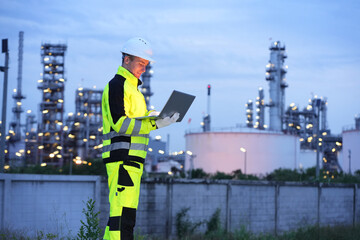 Petrochemical or refinery industry engineer working on laptop computer inspection petroleum oil refinery plant construction site. Engineering technician maintaining energy power gas system.