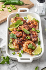 Spicy grilled chicken thighs roasted with chilli and lime on white dish, light gray kitchen background