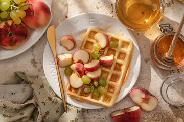 Breakfast belgian waffles with fruit and honey. Homemade healthy waffles on kitchen table in bright morning light, top view