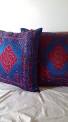 Two decorative cushions, royal blue with maroon/crimson patterns,  square, ornate design