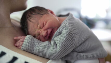 Newborn baby resting on mother's chest, visibly uncomfortable, expressing displeasure with a...