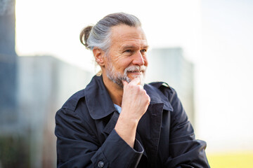 Mature man in dark coat smiling thoughtfully with hand on chin