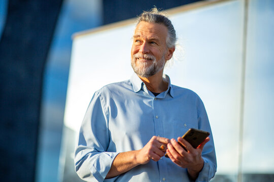 Smiling senior man using smartphone outdoors in sunlight