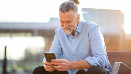 Elderly man using smartphone while sitting outdoors in city